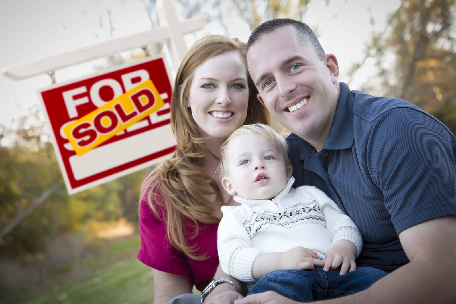 young couple in front of a sold real estate sign